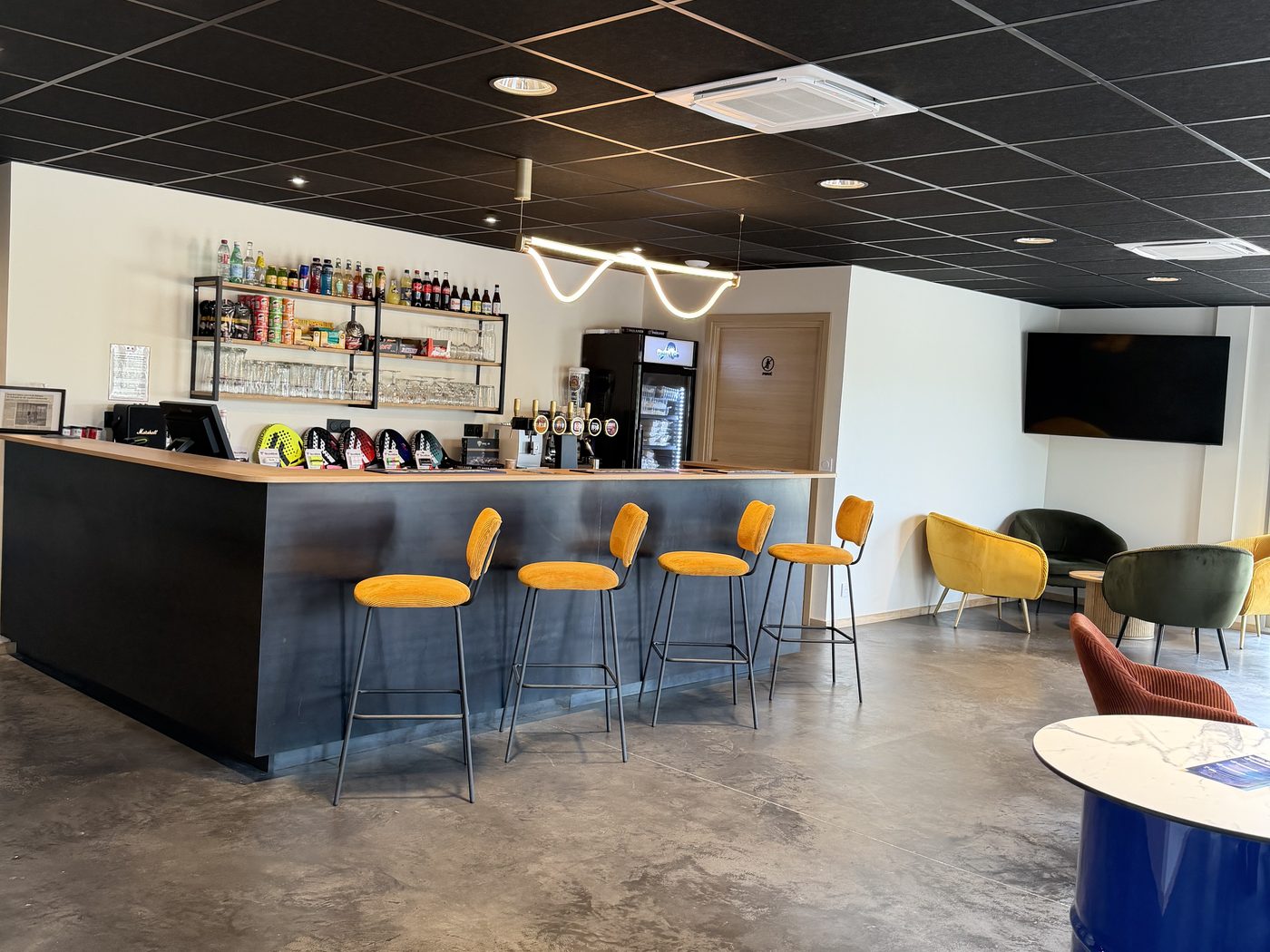 Le bar du club-house, comptoir noir et tabourets jaunes