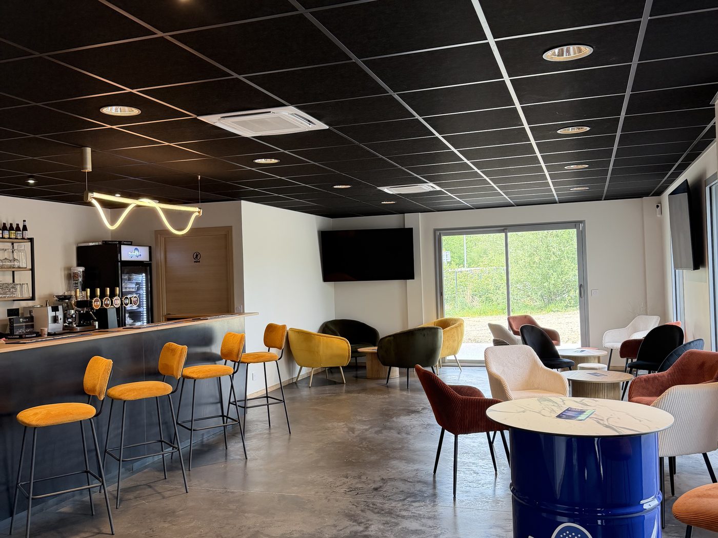 Le club-house et son bar, tabourets jaunes et fûts bleus Padel and Co