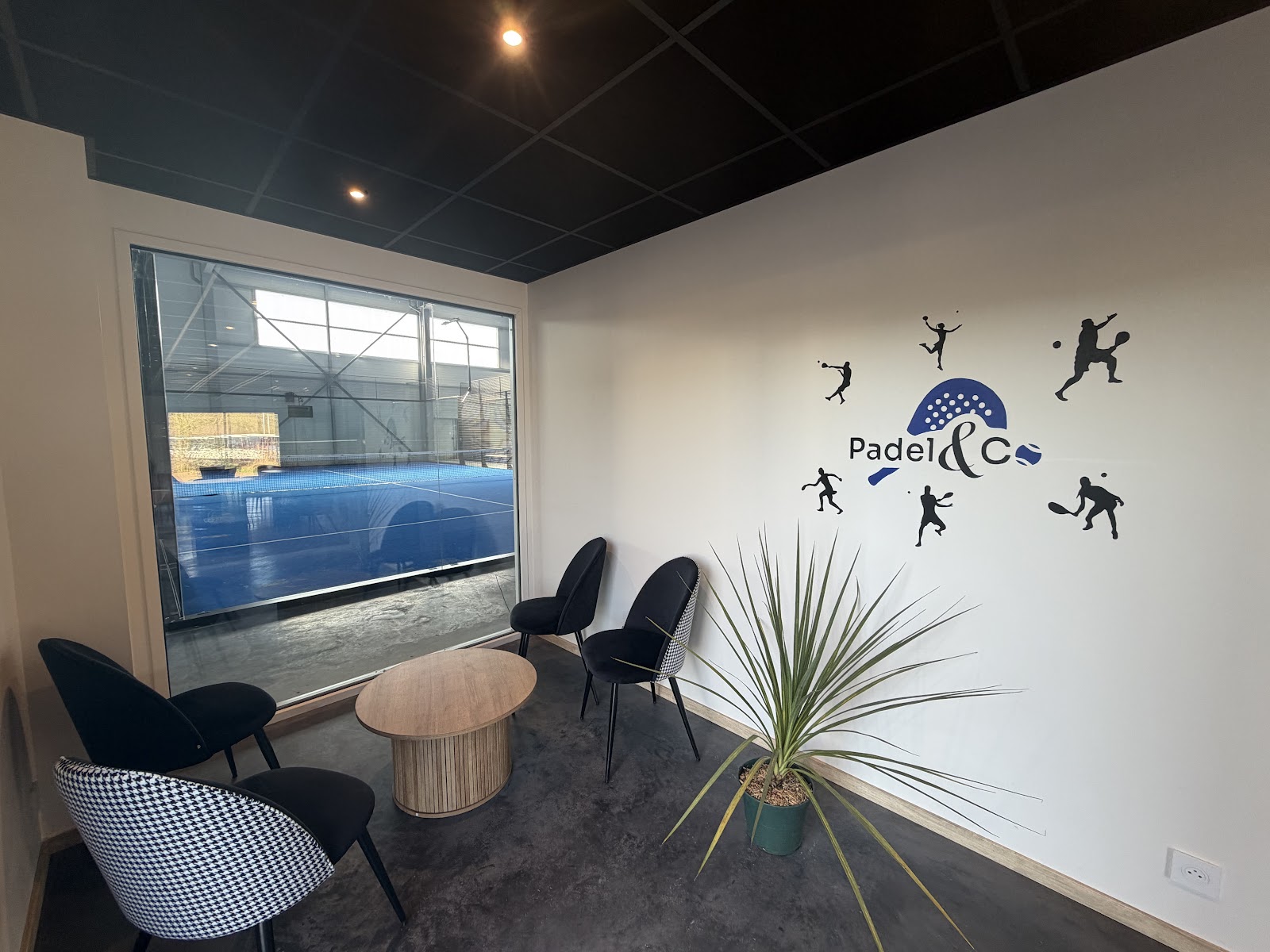 Le salon du club-house, mur au logo Padel & Co et vue directe sur les pistes